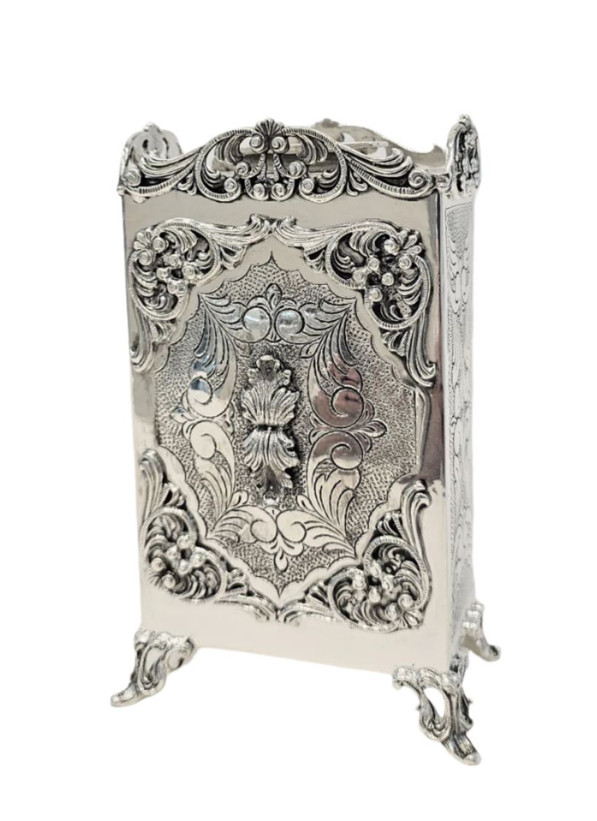 Decorative sterling silver tzedakah box with intricate floral patterns on a white background