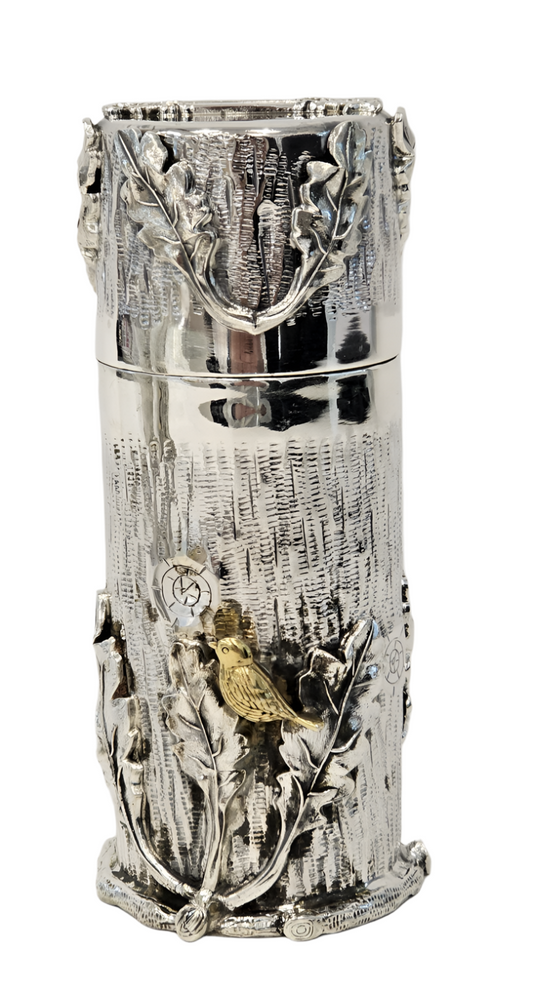 A sterling silver Tzedakah box with embossed tree and leaf patterns, featuring a lid with a small bird perched on a branch.
